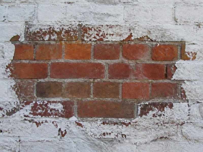 Peeling paint and a test removal area exposing the original fired brick surface in Fort Worth, Texas.
