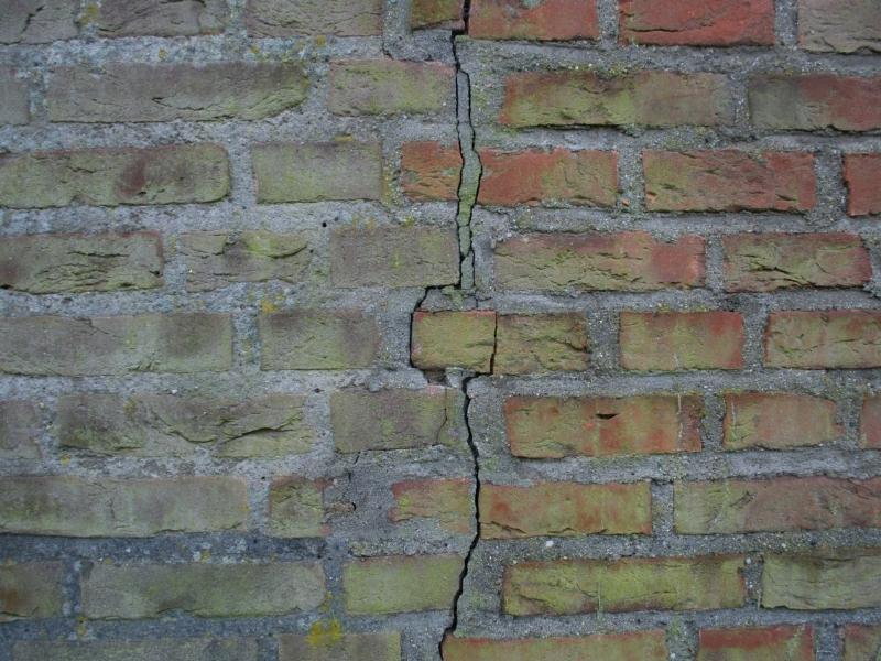 Masonry contractor inspecting cracks in a brick home exterior in Fort Worth, Texas, after a heatwave.
